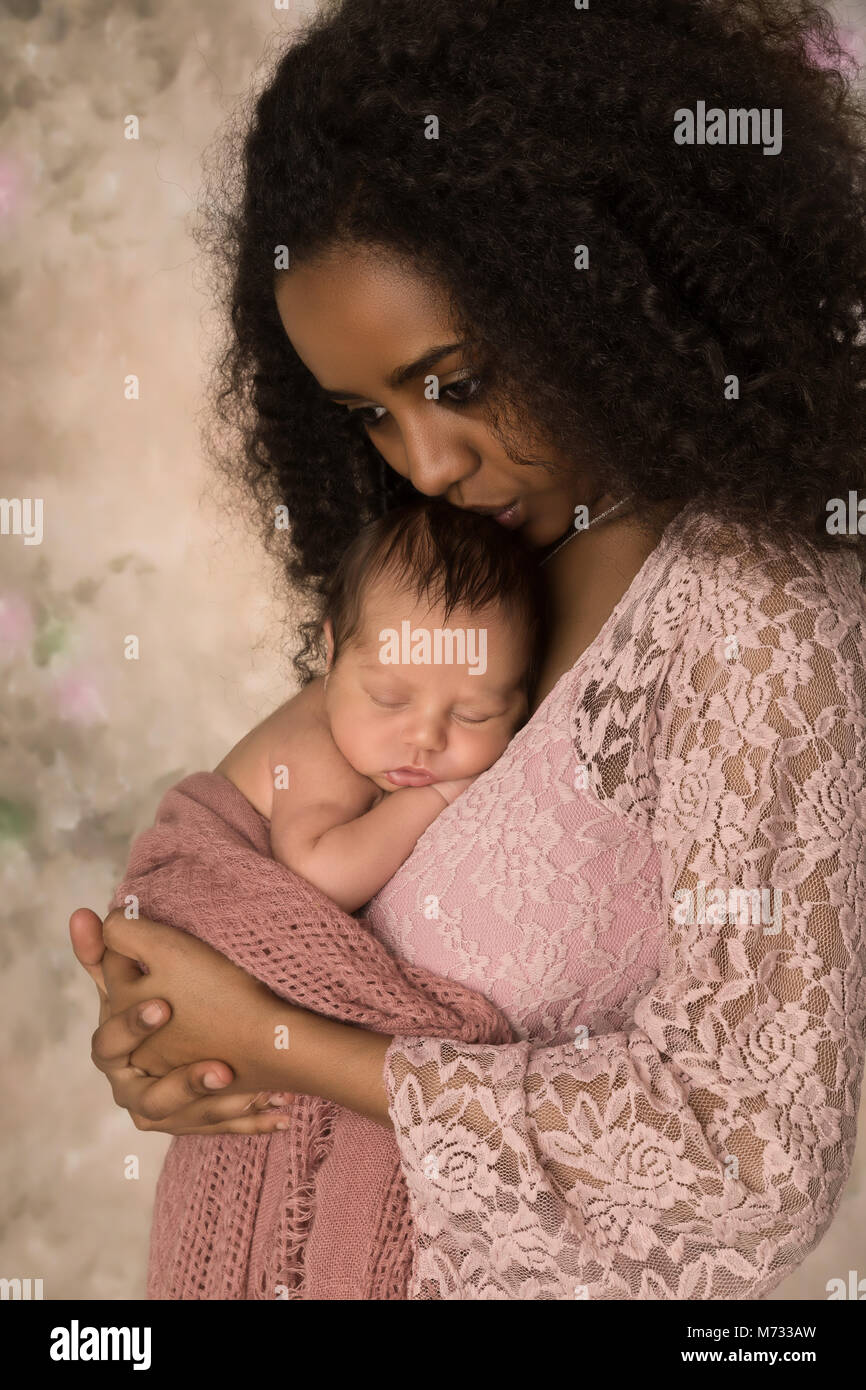 Schöne afrikanische Mutter im rosa Spitzenkleid hält ihr 1 Woche altes kleines baby Stockfoto