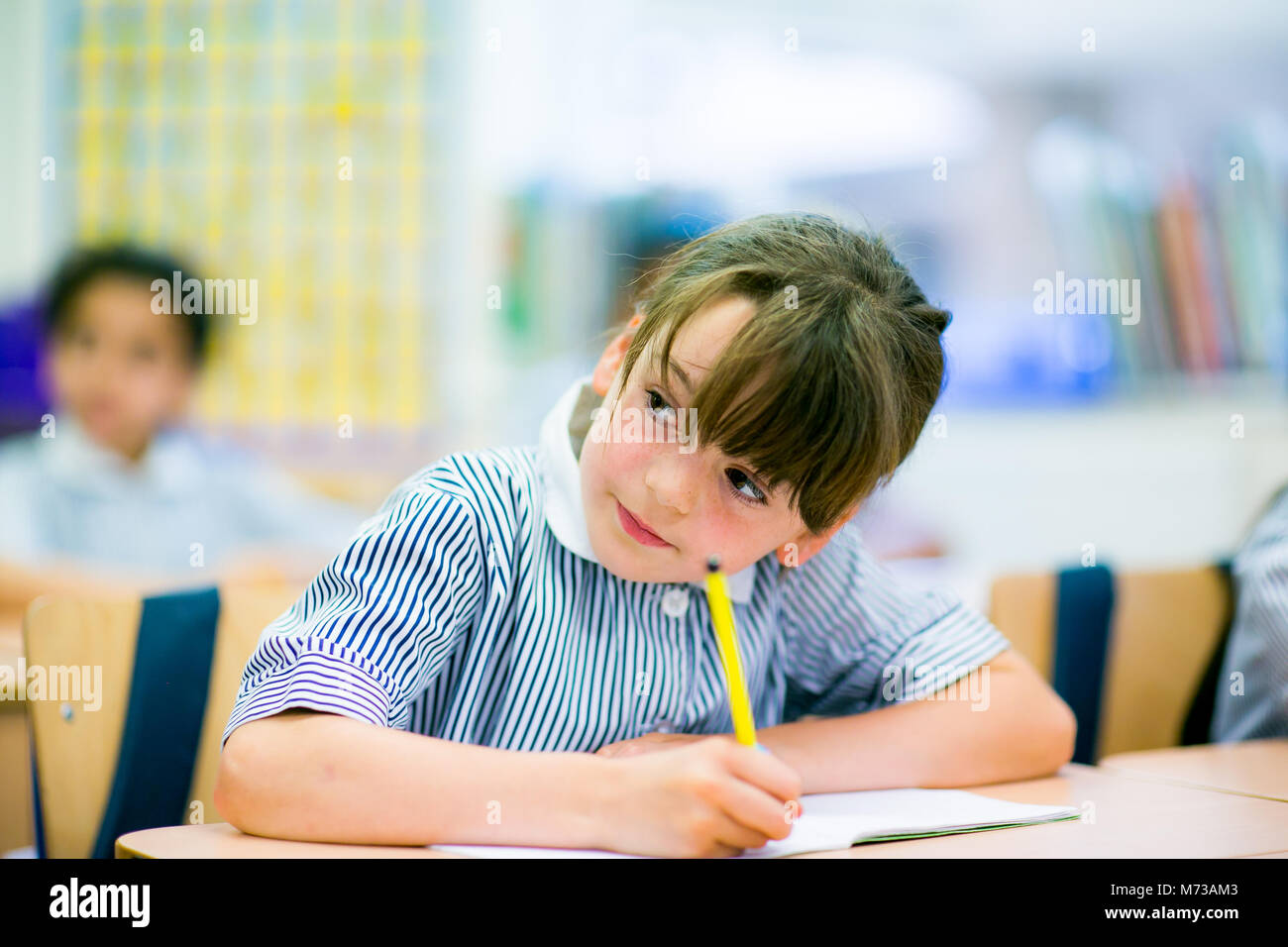 Primäre Schülerin an einem Schreibtisch sitzend mit einem Bleistift Stockfoto
