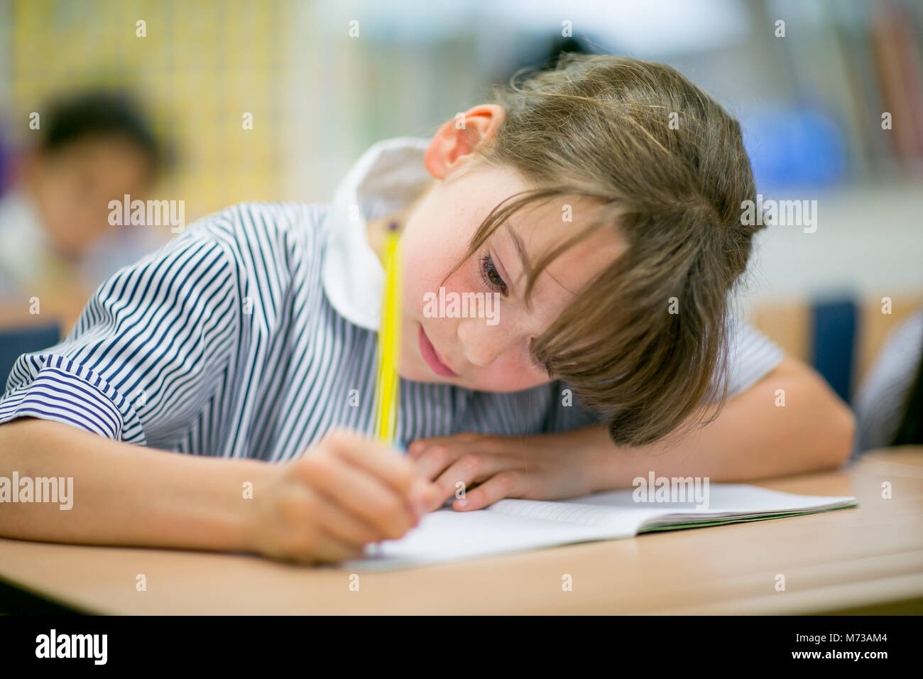 Primäre Schülerin an einem Schreibtisch sitzend mit einem Bleistift Stockfoto
