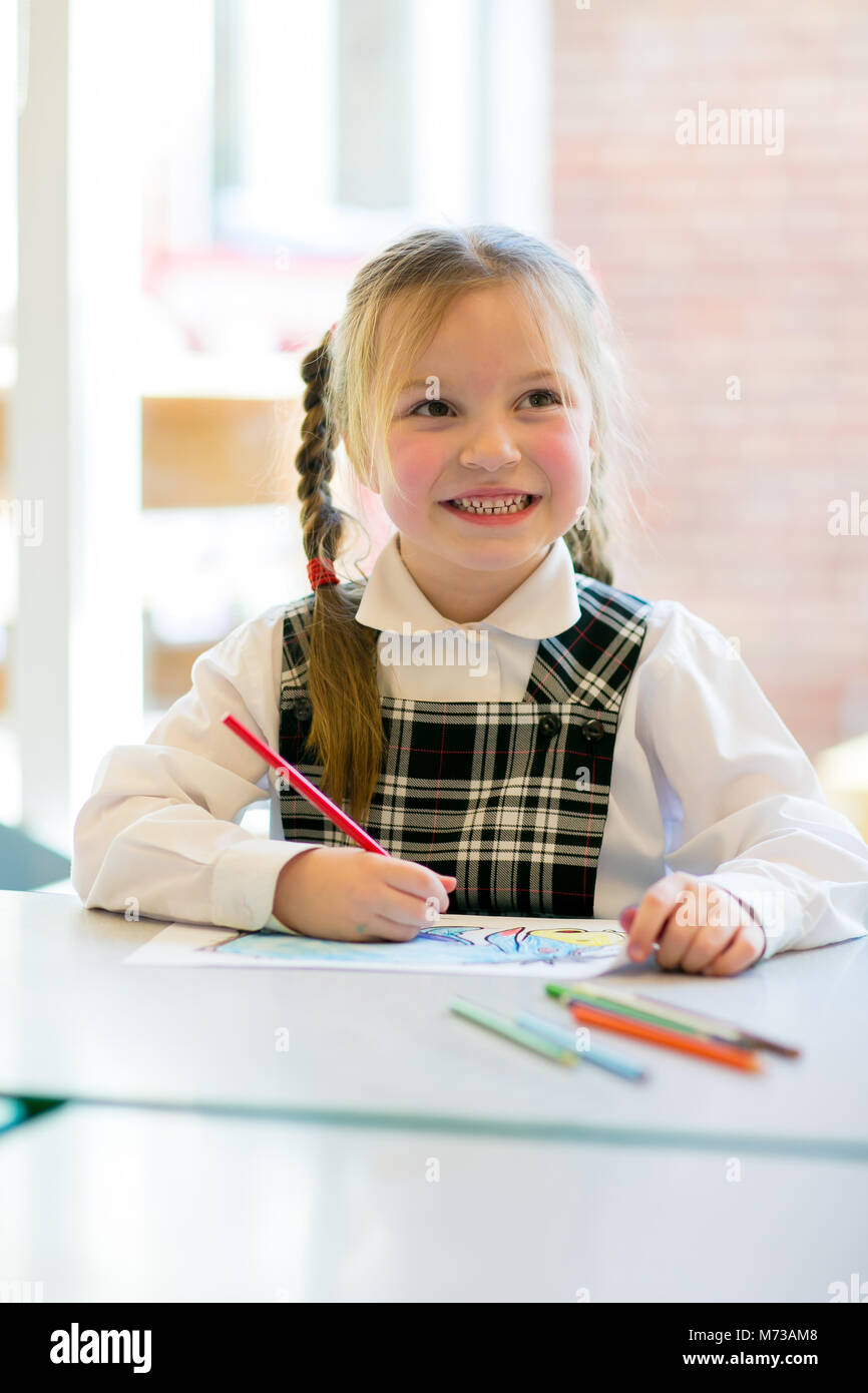 Primäre Schülerin an einem niedrigen Tisch Zeichnung sitzen, bis sie lächelnd mit einem Bleistift in der Hand. Stockfoto