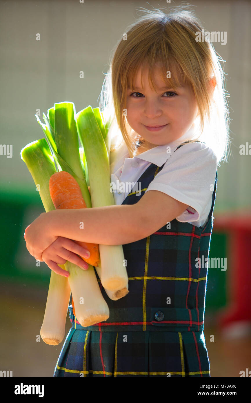 Grundschule Mädchen, umklammerte eine armvoll von Gemüse Stockfoto