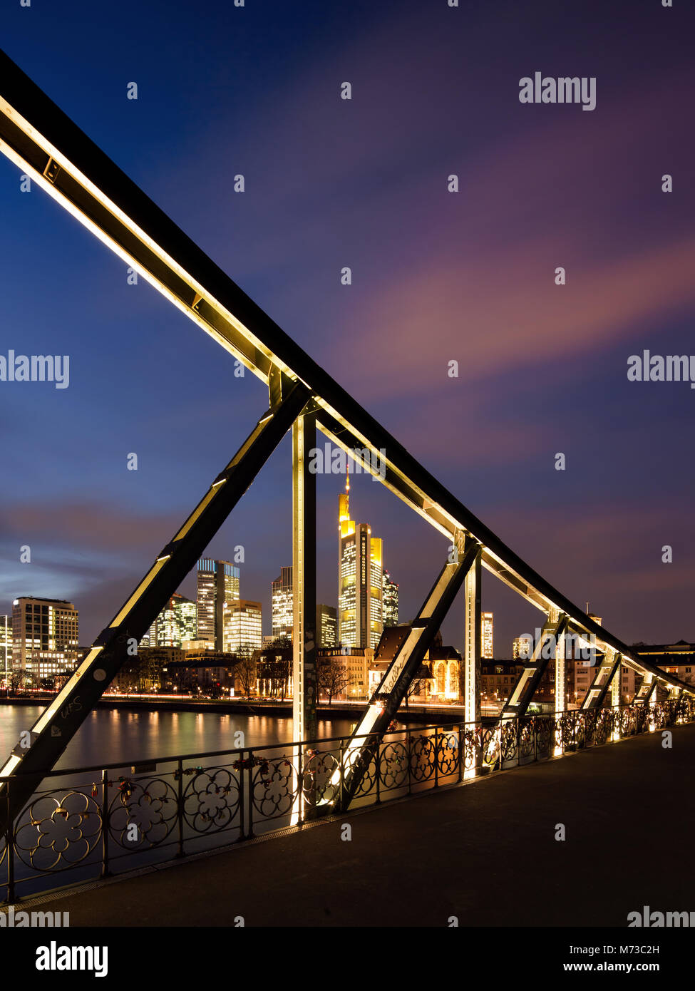 Skyline von Frankfurt am Main, Deutschland, durch die stählernen Trägern der "Eiserner Steg" Fußgängerbrücke über den Main in der Abenddämmerung gesehen. Stockfoto