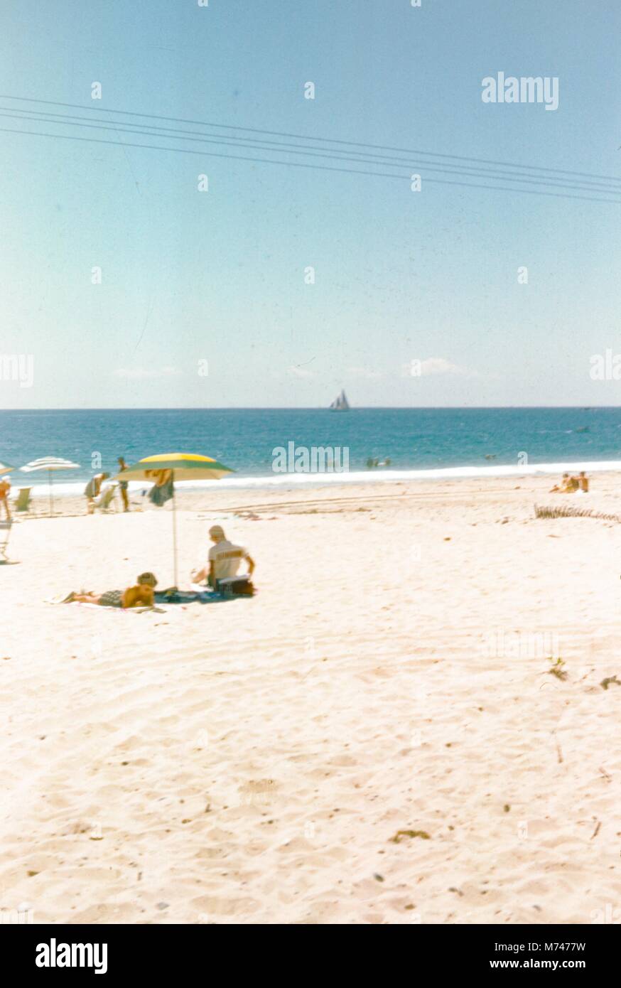 Verschiedene Gruppen von Menschen am Strand zu entspannen, ein großes Segelboot kann in der Ferne, 1955 gesehen werden. () Stockfoto