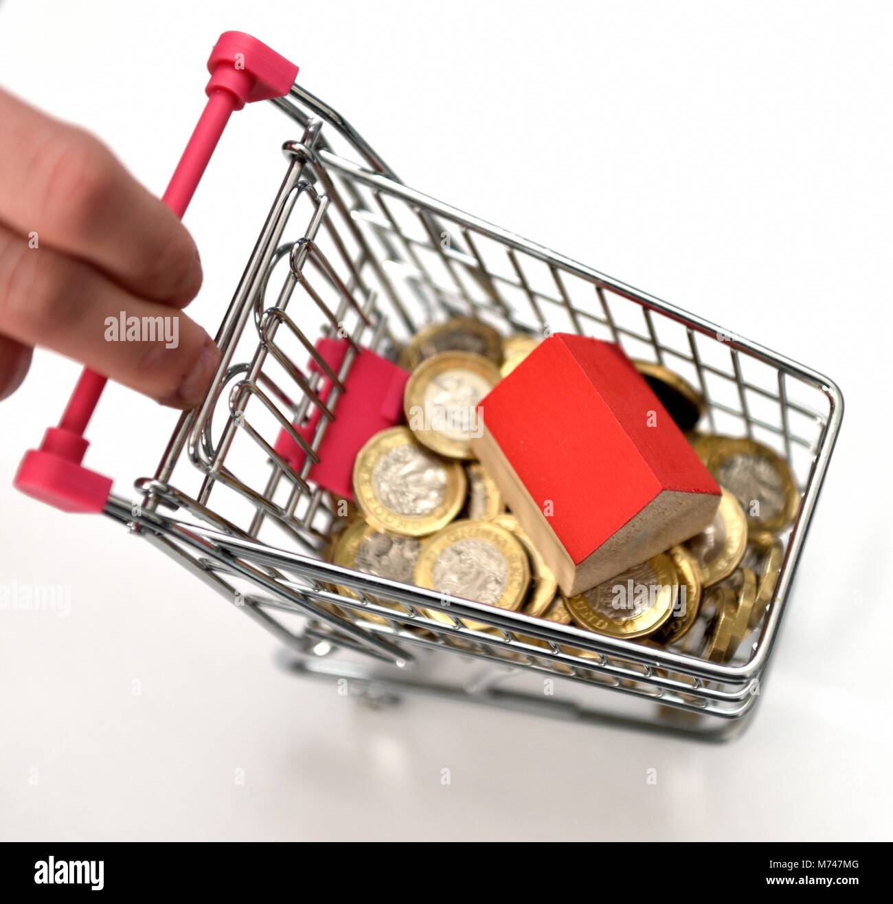Ein kleines Haus in einer Miniatur Einkaufswagen mit einem Pfund Münzen Haus Konzept kaufen Stockfoto