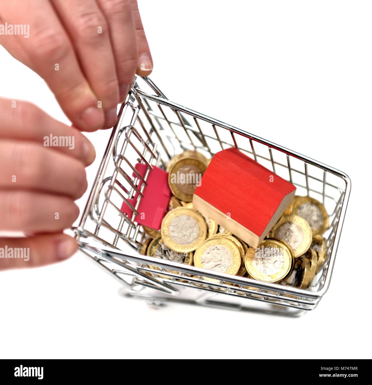 Ein kleines Haus in einer Miniatur Einkaufswagen mit einem Pfund Münzen Haus Konzept kaufen Stockfoto