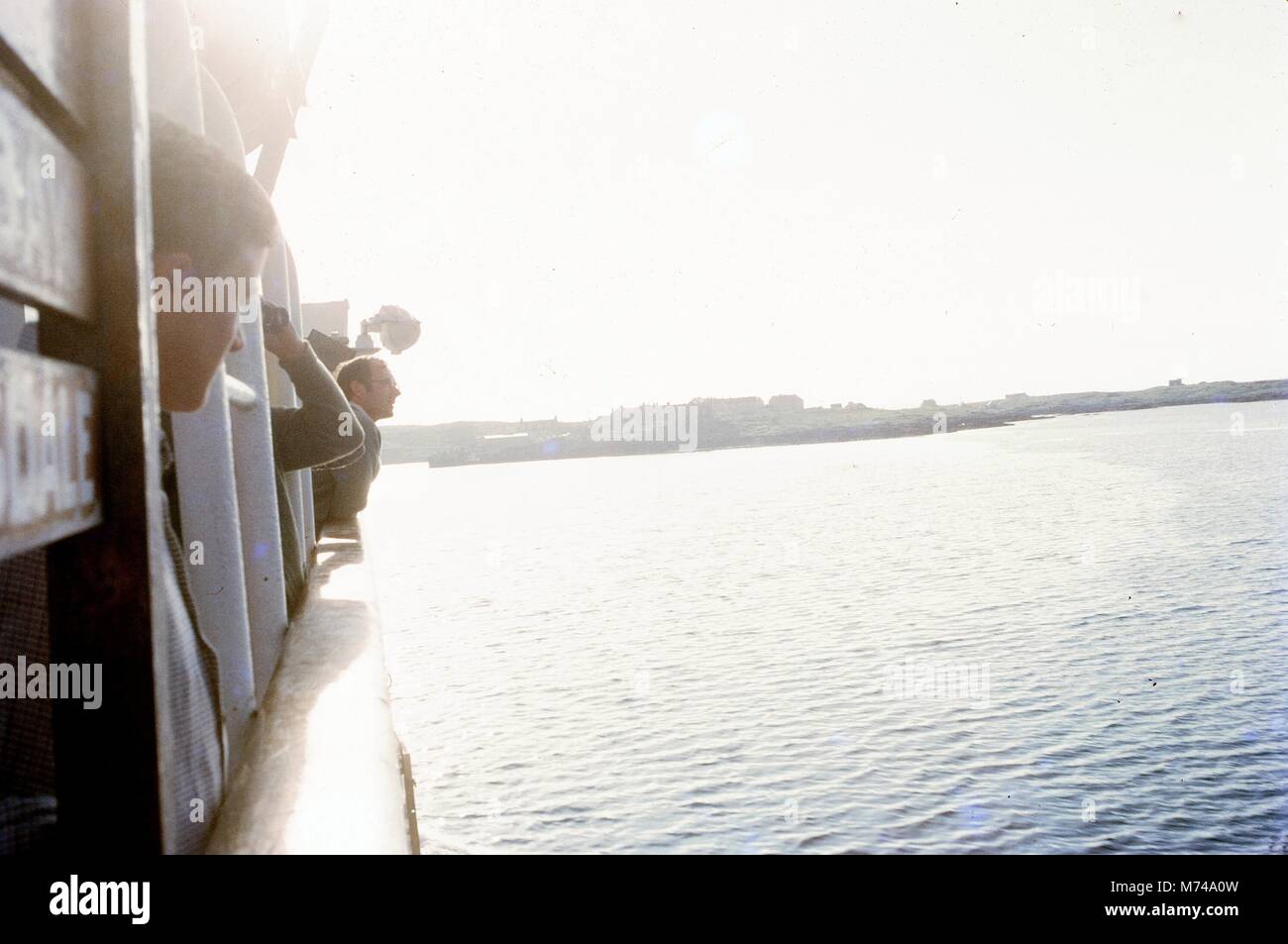 Die Leute stehen an der Seitenschiene auf einem Boot über den Rand zu schauen, wie Sie über einem Körper von Wasser, 1965 reisen. () Stockfoto
