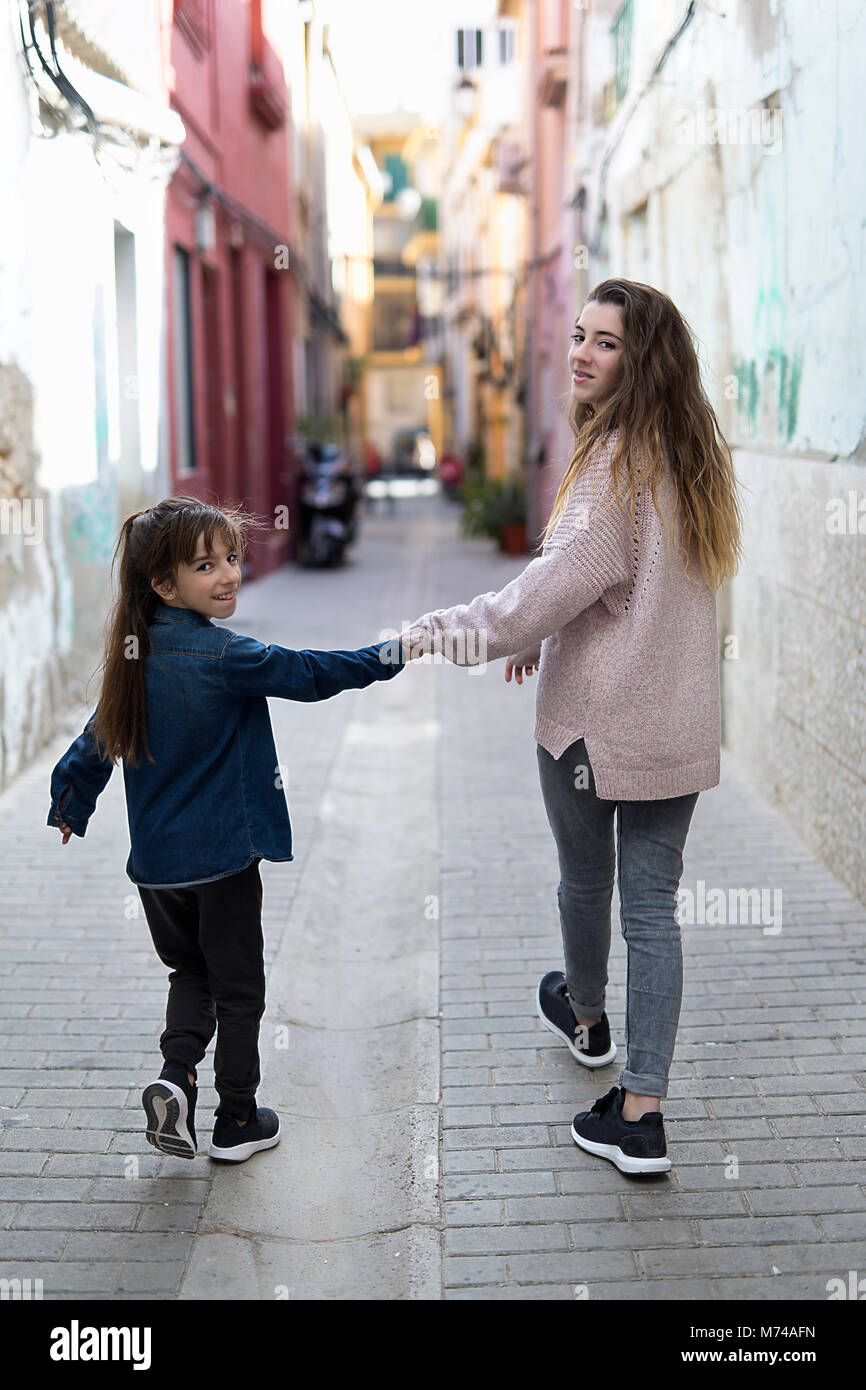 Schwestern gehen Hand in Hand durch eine Straße in Orihuela, um die Kamera zu verbinden. Stockfoto