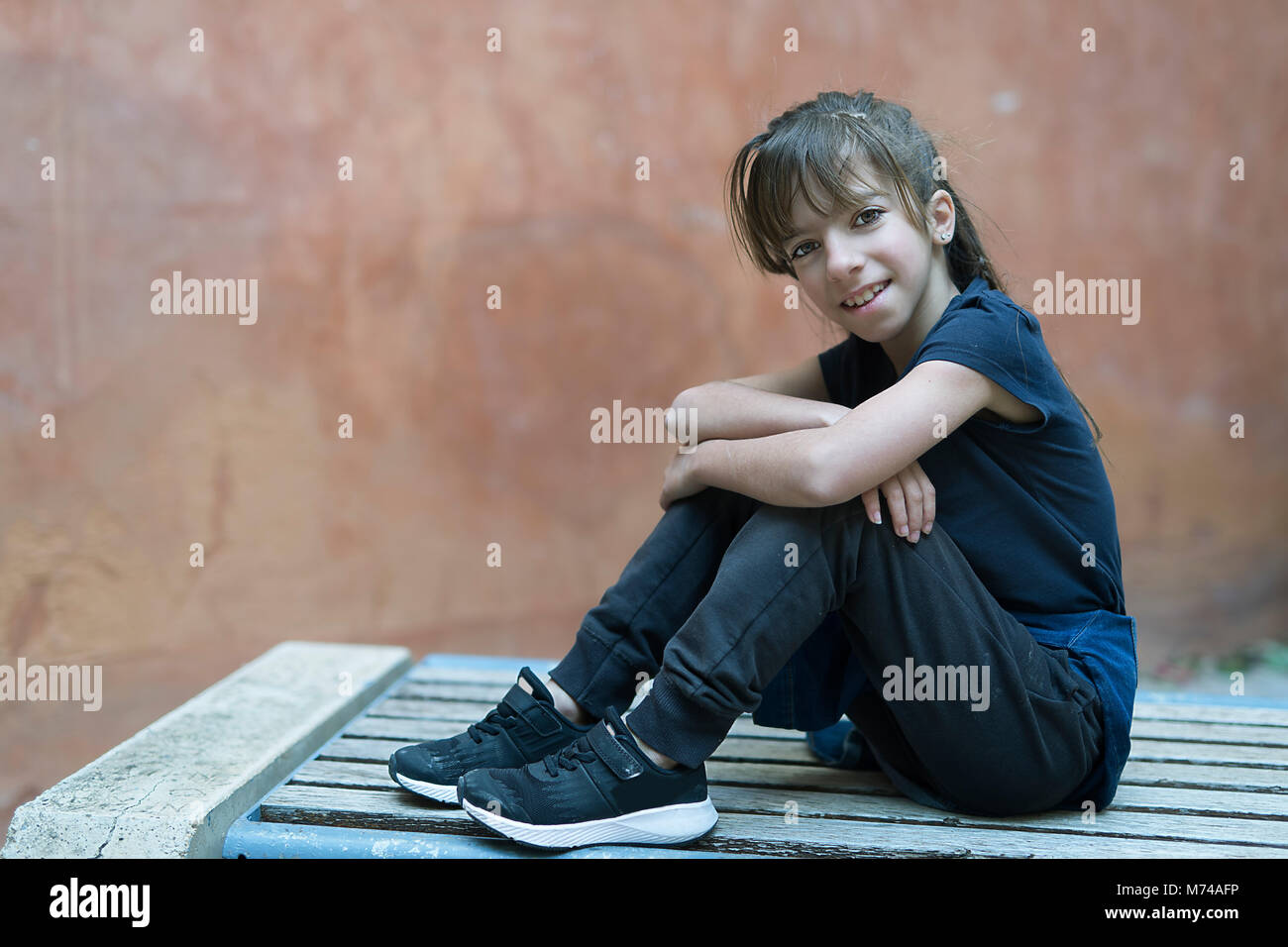 10 Jahre alte Mädchen sitzt auf einer Holzbank an der Kamera mit einem Lächeln. Stockfoto