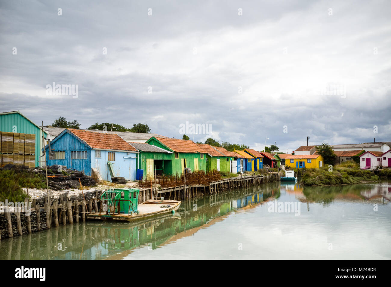 Reihe von bunten Oyster Schuppen mit flachem Boden oyster Boote in einem kleinen Dorf auf der Insel Oleron, Frankreich, im Rahmen einer stürmischen Sommer Himmel. Stockfoto