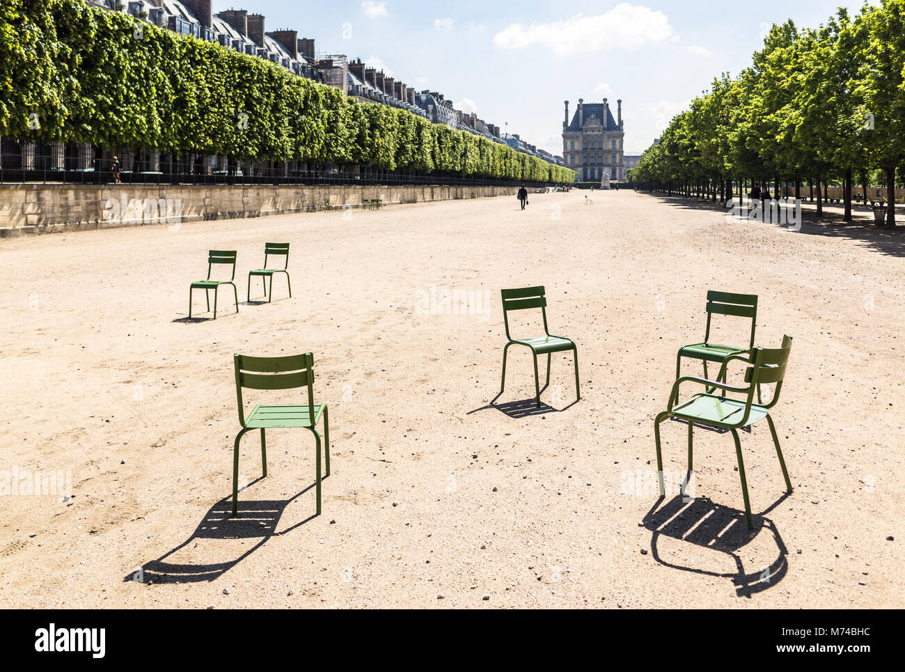 Grüne Metallstühle in einer breiten Allee im Tuileries-Garten in Paris, Frankreich, mit dem Louvre-Palast in der Ferne. Stockfoto