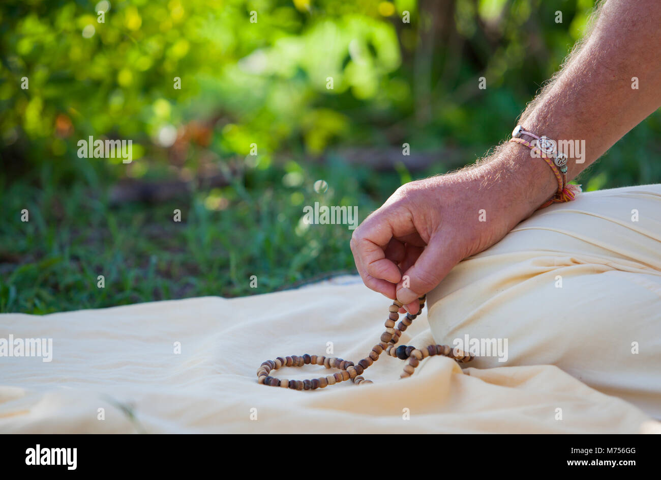 Eine Nahaufnahme an Hand des Menschen üben Meditation mit mala Perlen, ausserhalb auf Gras. Er ist ein om Armband auf seinem Arm. Stockfoto