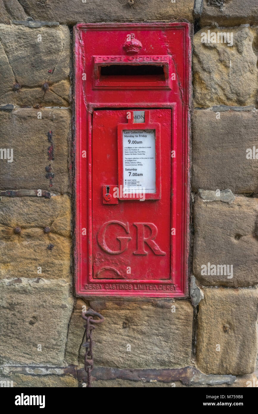 Alte rote Wand montiert Britische Post Ofice Post Box auf einer Sandsteinmauer mit Krone und Zeit Tabelle Stockfoto