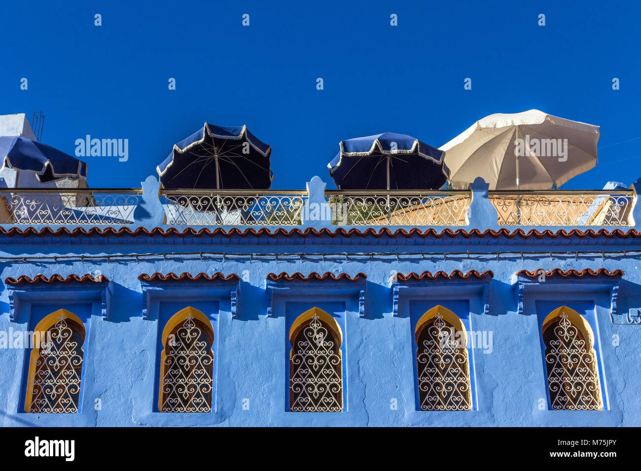 Blick auf terrassenförmig angelegten Sonnenterrasse über eine Reihe von dekorativen Fenstern und architektonische Merkmale gegen den tiefblauen Himmel. Chefchaouen, Marokko Stockfoto