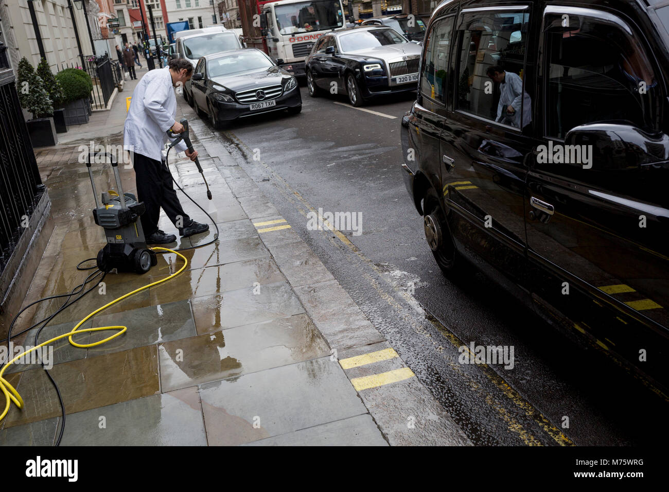 Nach einer Woche Schnee und Eis, ein Angestellter benutzt ein Druck Schlauch nach unten eine schmutzige Pflaster am Seiteneingang des Wolseley Brasserie gegenüber dem Ritz in Arlington Street zu waschen, am 5. März 2018 in London, England. Stockfoto