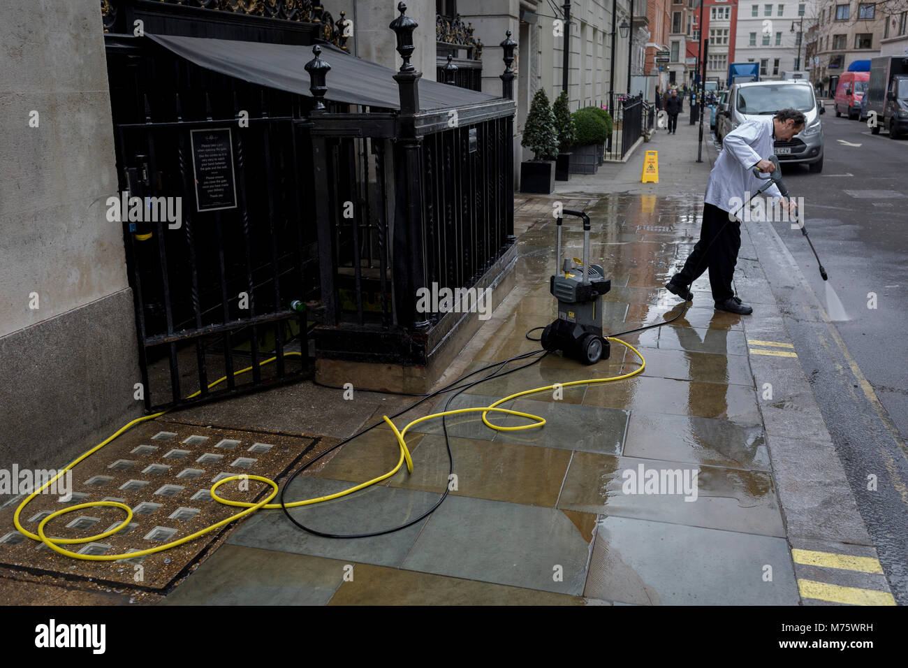 Nach einer Woche Schnee und Eis, ein Angestellter benutzt ein Druck Schlauch nach unten eine schmutzige Pflaster am Seiteneingang des Wolseley Brasserie gegenüber dem Ritz in Arlington Street zu waschen, am 5. März 2018 in London, England. Stockfoto