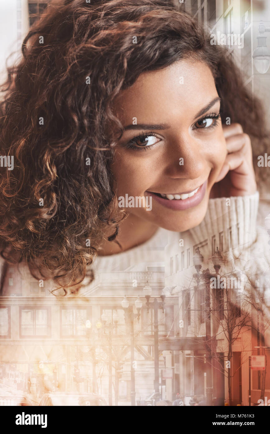 Angenehme fröhliche Frau, die gerne beim Sitzen und Lächeln Stockfoto