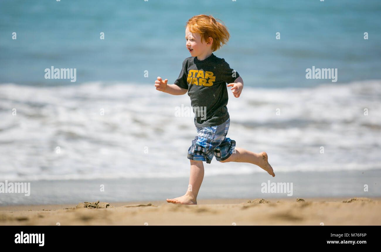 Rothaarige Junge laufen am Strand entlang, am Rande des Wassers Stockfoto