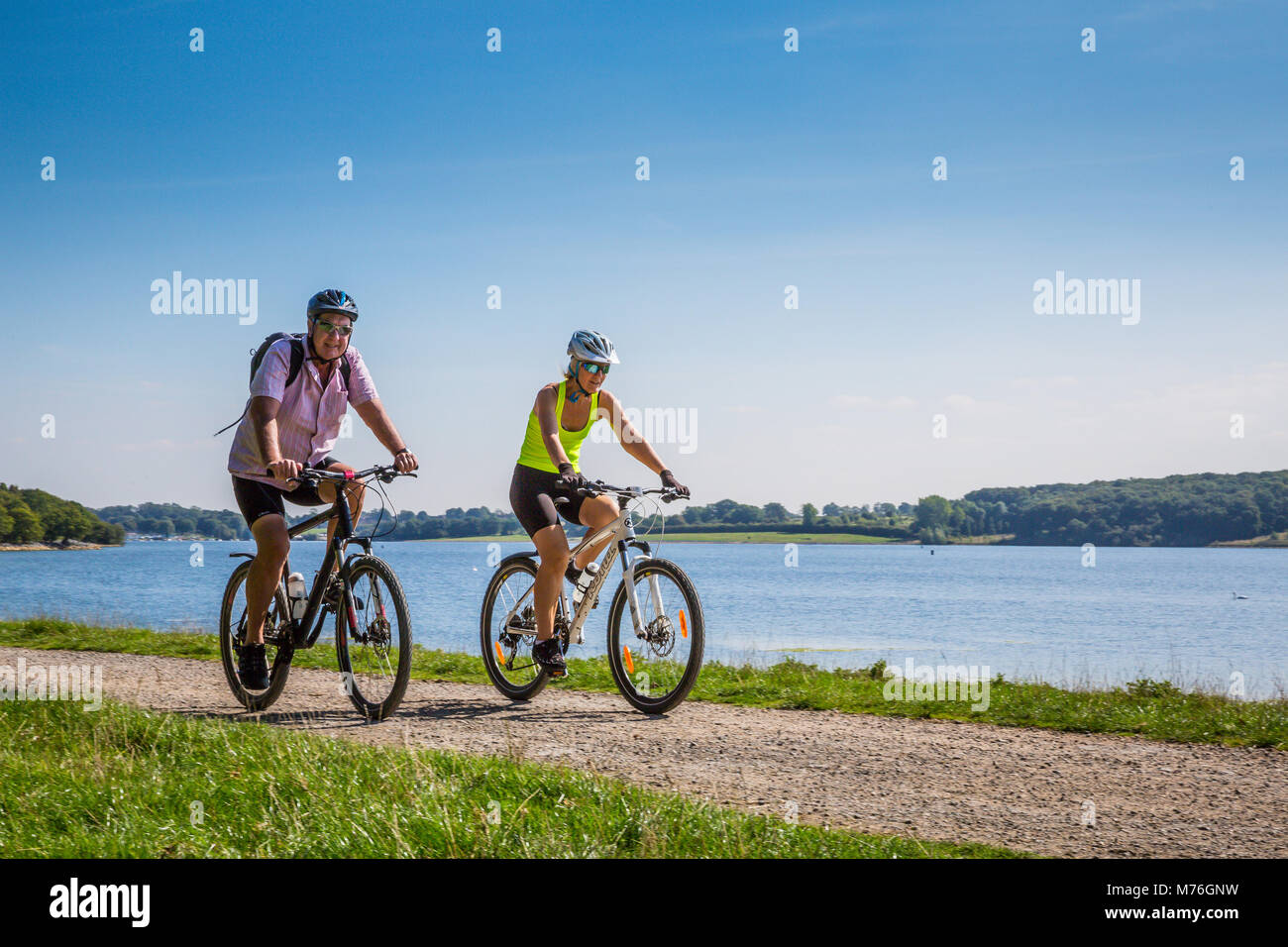 Mann und Frau, ihre Mountainbikes entlang einem Pfad am See bei schönem Wetter Stockfoto