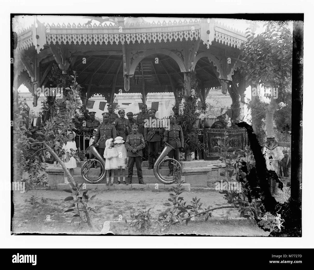 Ein historisches Foto einer Band, die in einem Pavillon auftritt, begleitet von jungen Frauen. Das Bild spiegelt eine Gemeindeversammlung in einem öffentlichen Park oder einer Umgebung im Freien wider. Stockfoto