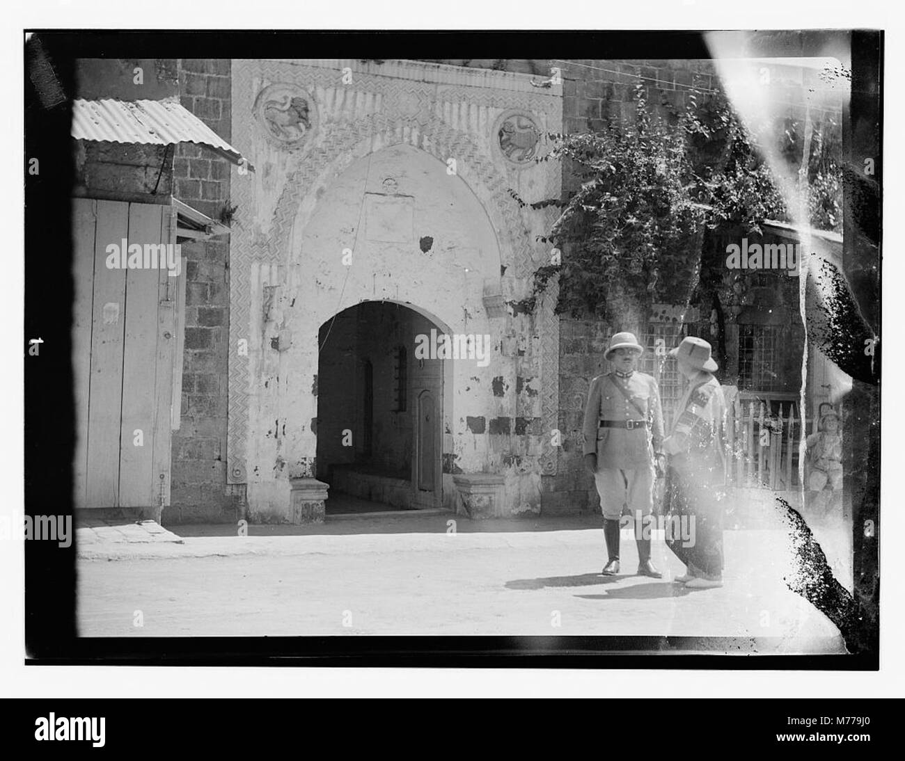 Dieses Foto zeigt zwei Männer, die vor einem Steintor stehen, das mit Löwenreliefskulpturen geschmückt ist, und hebt die architektonischen Details und die symbolische Verwendung von Tierbildern bei der Torgestaltung hervor. Stockfoto