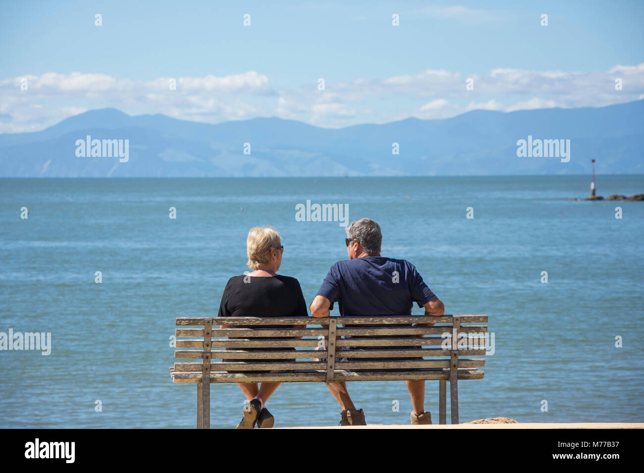 Älteres Paar sitzt auf der Bank auf kaiteriteri Beach, Kaiteriteri, Tasman, Neuseeland Stockfoto