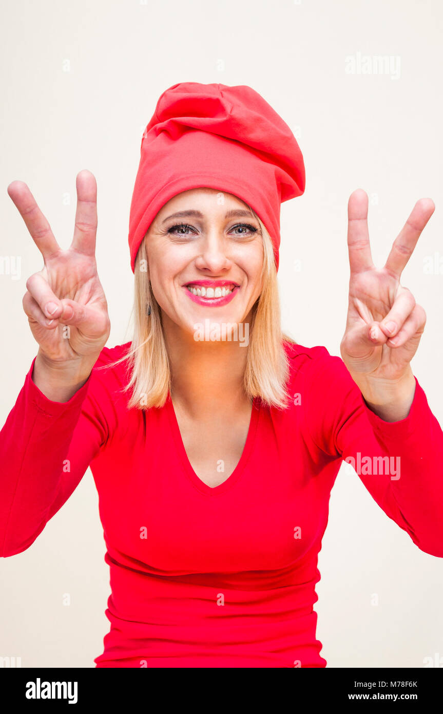 Glücklich lächelnde Red Hat und Langarm Shirt blonde Frau mit zwei Fingern disco Sieg Freiheit, Frieden hand Zeichen auf weißem Hintergrund. Stockfoto