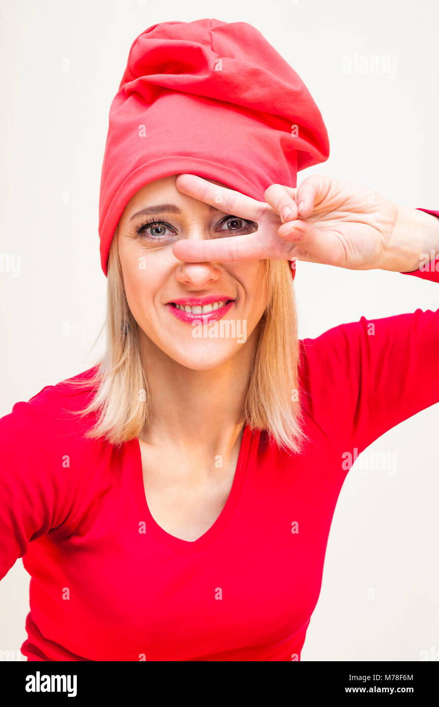 Glücklich lächelnde Red Hat und Langarm Shirt blonde Frau mit zwei Fingern disco Sieg Freiheit, Frieden hand Zeichen auf weißem Hintergrund. Stockfoto