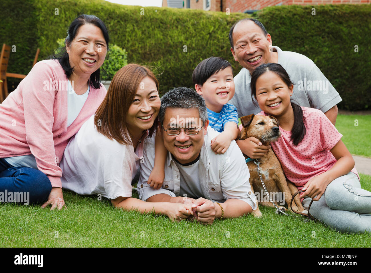 Happy Family Portrait. Chinesischen Familie gibt, die auf dem Gras in Ihrem Garten, Lächeln für die Kamera mit Ihrem Haustier Hund. Stockfoto