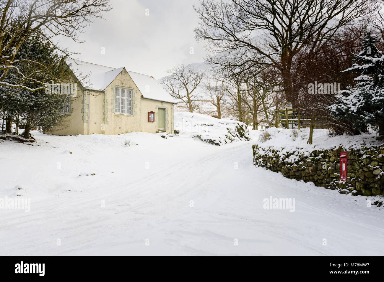 Winter verschneite Straße vorbei an der alten Schule, jetzt das Dorf Halle im Buttermere im englischen Lake District Stockfoto