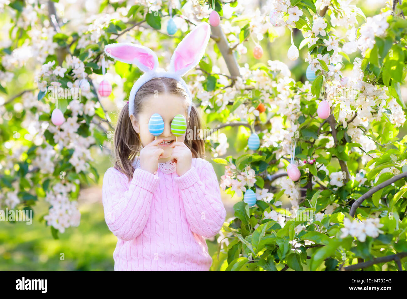 Kind auf Ostereiersuche im blühenden Kirschbaum Garten mit Blumen. Kind mit farbigen Eier im Korb. Kleines Mädchen mit Hasenohren. Ostern deco Stockfoto