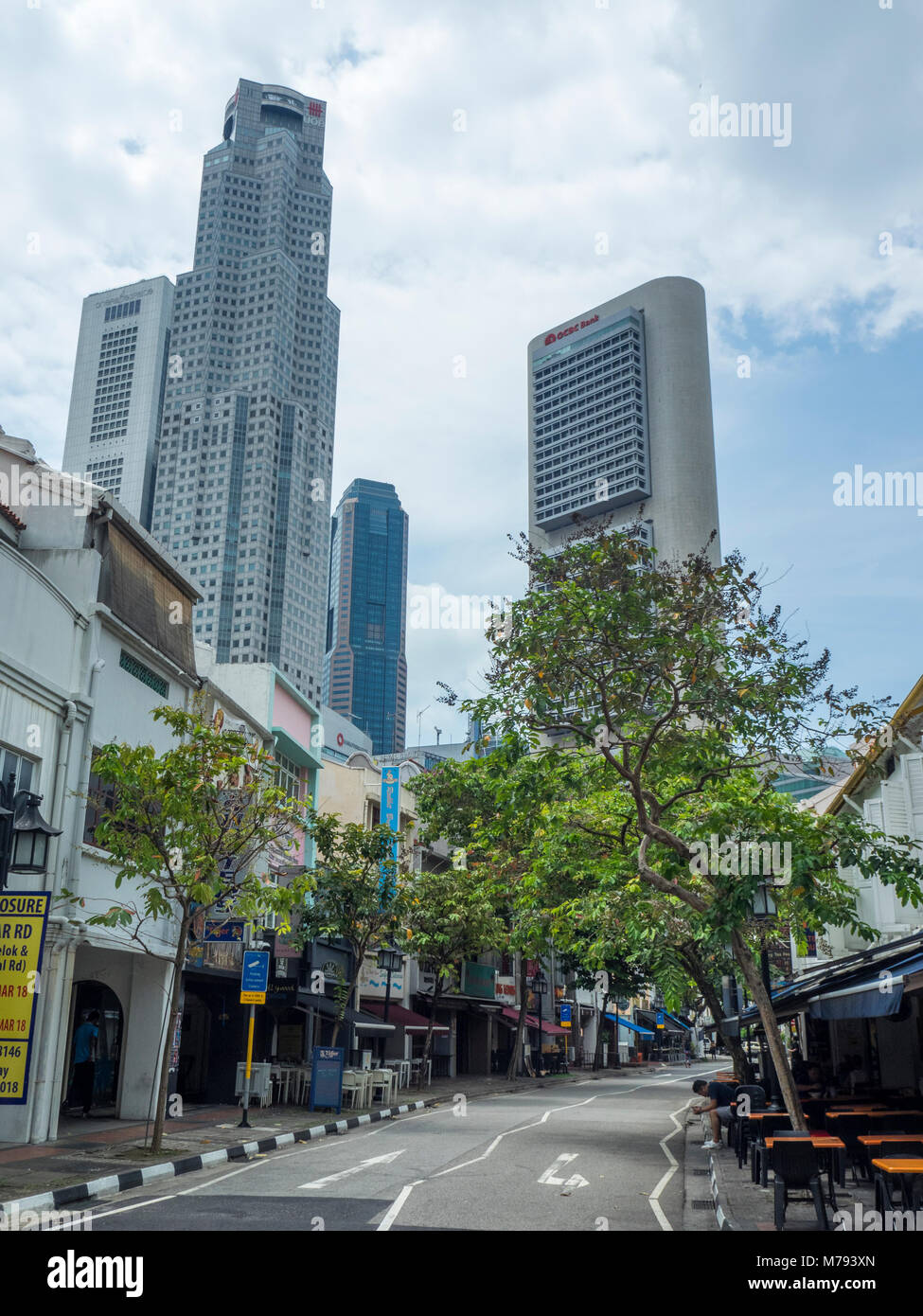 Von Bäumen gesäumten Circular Road, und die Reihe der traditionellen Shophouses kontrastieren mit den Wolkenkratzern der Innenstadt von Singapur. Stockfoto