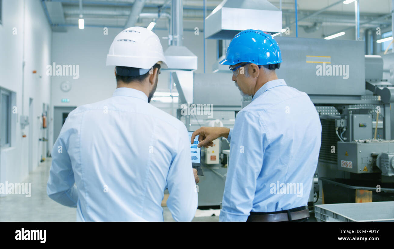 Rückansicht der Leiter des Projekts hält Laptop und Diskutieren Produkt Details mit Chief Engineer, während Sie durch moderne Fabrik gehen. Stockfoto