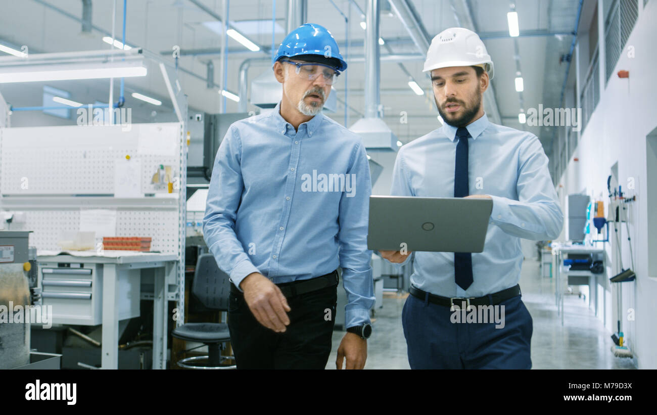 Leiter der Abteilung hält Laptop und Diskutieren Produkt Details mit Chief Engineer, während Sie durch moderne Fabrik gehen. Stockfoto