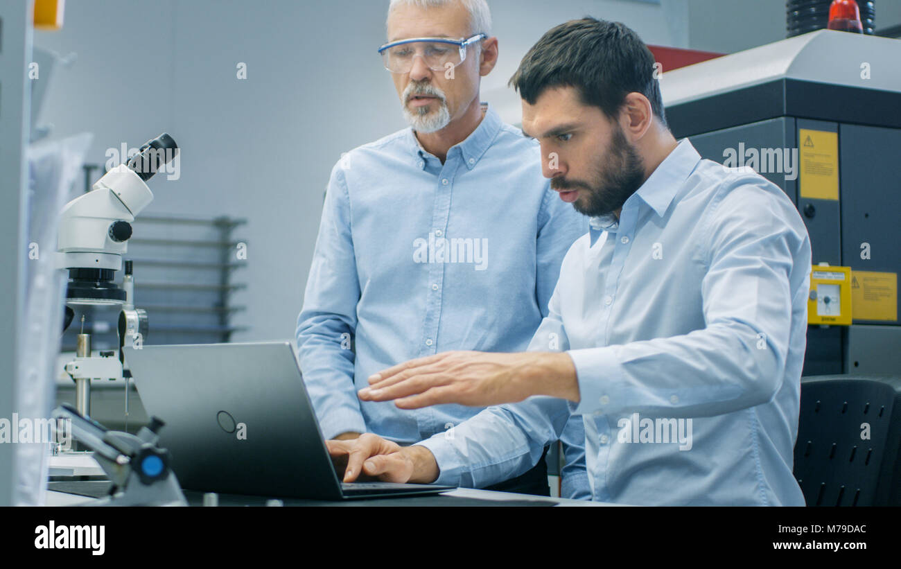 Zwei industrielle Wissenschaftler/Ingenieure/Techniker Diskussion haben während der Arbeit am Laptop. Im Hintergrund moderne Labor/Factory Stockfoto