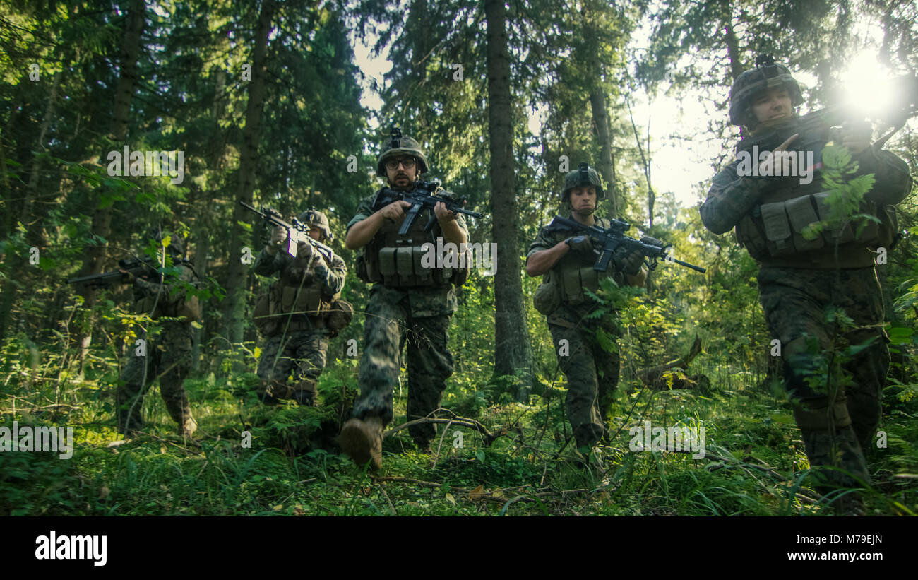 Gruppe von fünf voll ausgestatteten Soldaten in der Tarnung auf eine Aufklärung militärische Mission, Gewehre bereit. Sie bewegen sich in der Ausbildung durch den Wald. Stockfoto