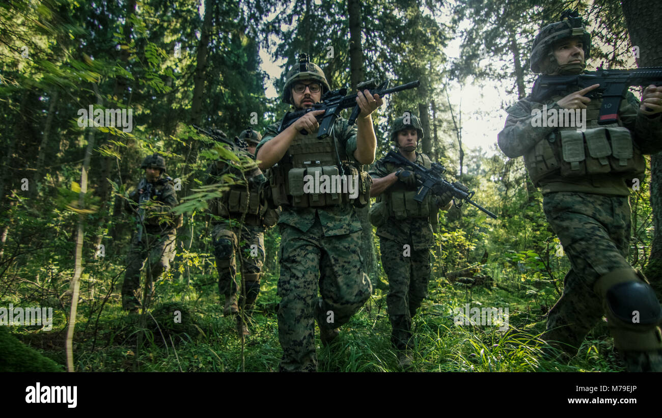 Kader von voll ausgestatteten Soldaten in der Tarnung auf eine Aufklärung militärische Mission, Gewehre bereit. Sie bewegen sich in Formation durch dichten Wald. Stockfoto