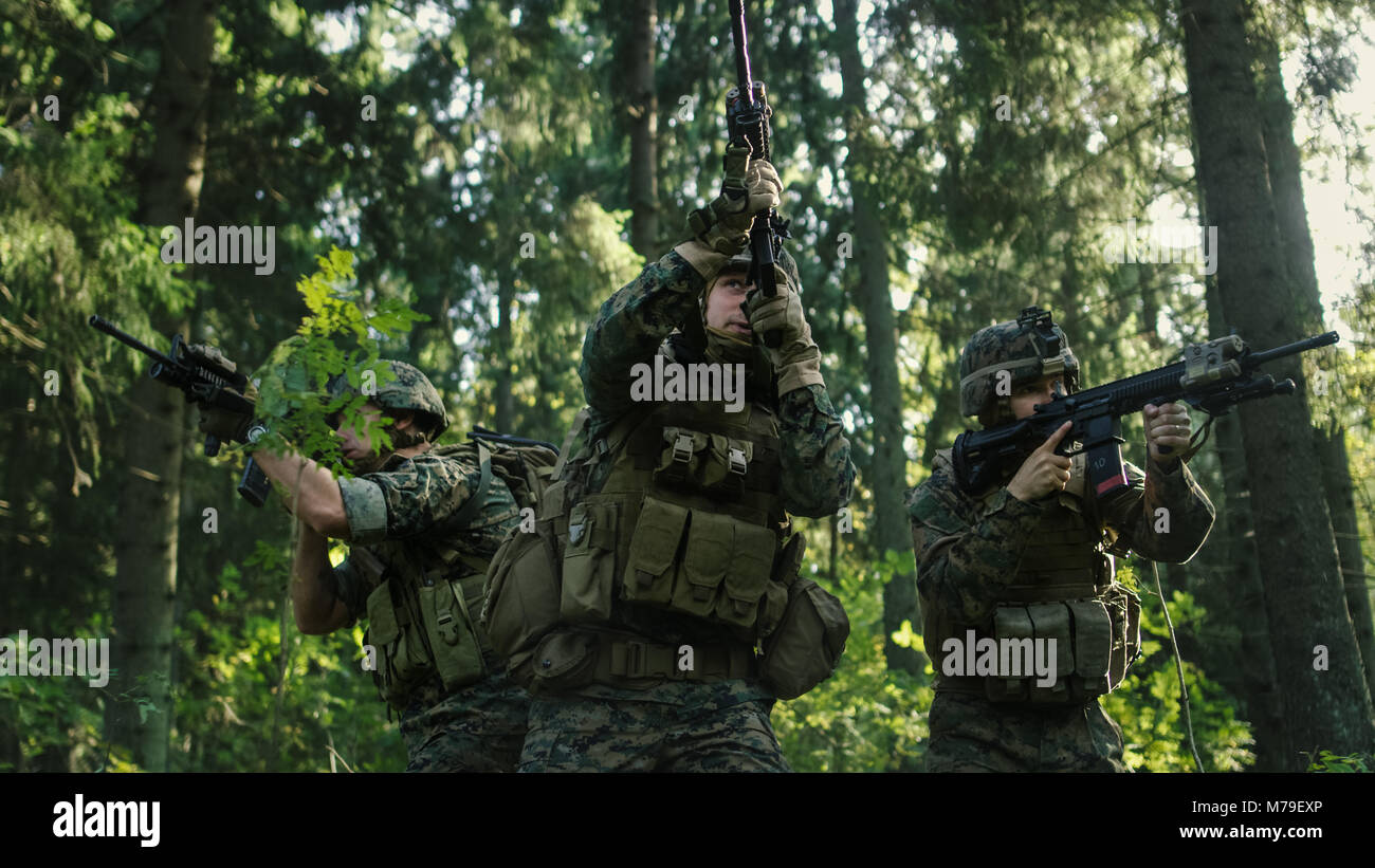 Drei voll ausgestatteten Soldaten tragen Camouflage Einheitliche angreifenden Feind, Sie in der Haltung, die Gewehre schießen. Militärische Operation. Stockfoto