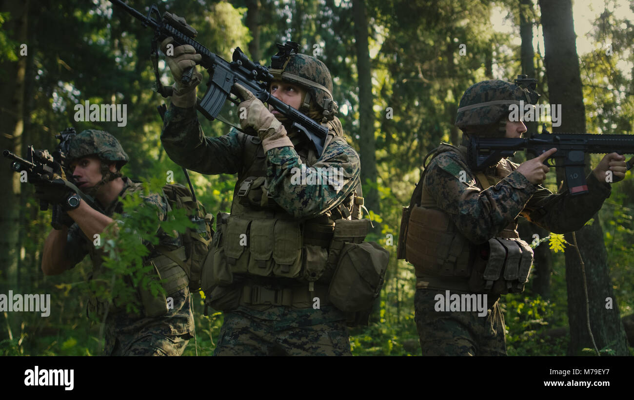 Voll ausgestattete Soldaten tragen Camouflage Einheitliche angreifenden Feind, Gewehre in Anschlag. Militärische Operation handeln, Gruppe durch den Wald zu laufen. Stockfoto