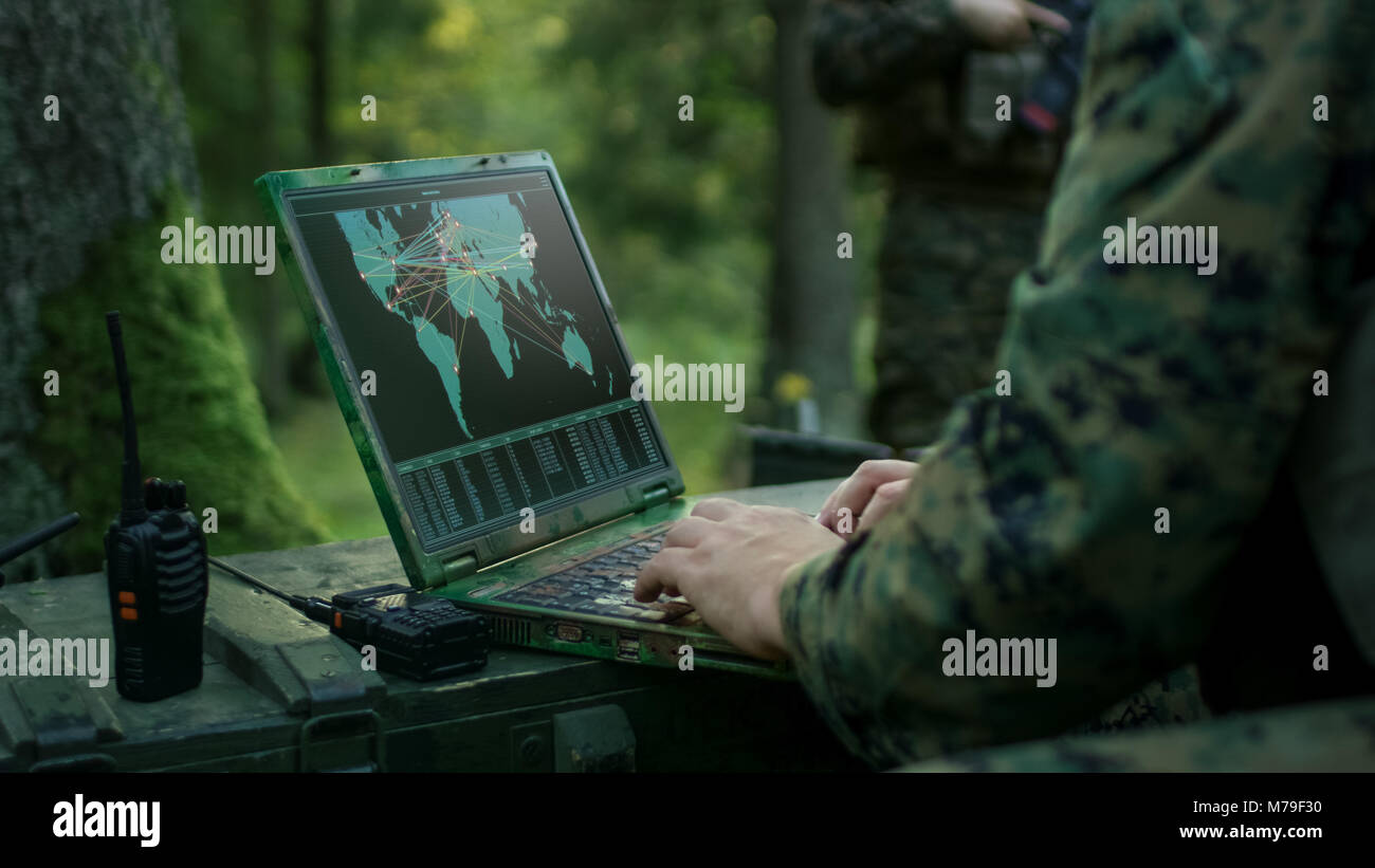 Militärische Operation in Aktion, Soldaten mit militärischen Grade Laptop Targeting Feind mit Satelliten. Im Hintergrund getarnt Zelt auf den Wald. Stockfoto