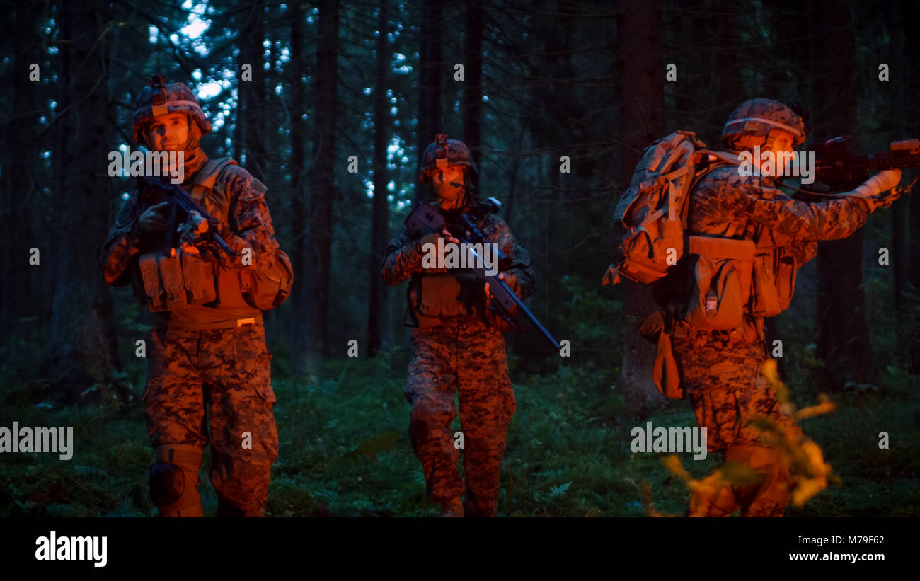 Gruppe von fünf voll ausgestatteten Soldaten in der Tarnung auf eine Aufklärung militärische Nacht Mission. Sie sind erleuchtet von roten Streulicht und durch dichten Wald bewegen Stockfoto