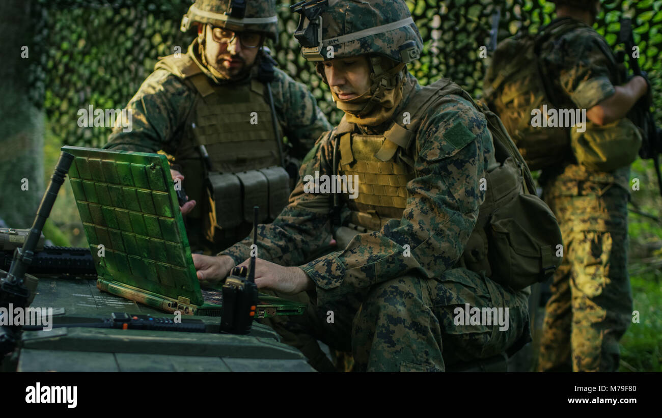Militärische Inszenierung Base, Offizier gibt Aufträge zu Chief Engineer, verwenden Sie Radio und Armee Grade Laptop. Sie sind in getarnt Zelt in einem Wald. Stockfoto