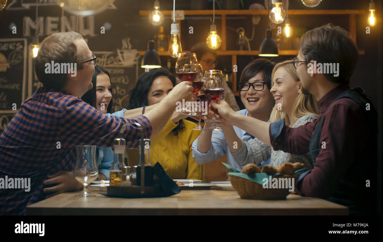 Vielfältige Gruppe von Freunde Feiern mit einem Toast und Clink angehoben Weingläser in der Feier. Schöne junge Leute haben Spaß in der stilvollen Bar Stockfoto