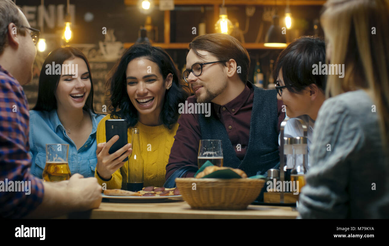 Schöne Hispanic Frau zeigt interessante Sachen auf Ihrem Smartphone zu Ihren Freunden während Sie gute Zeit in Bar. Sie Lachen, Scherzen, Getränk in der Bar Stockfoto