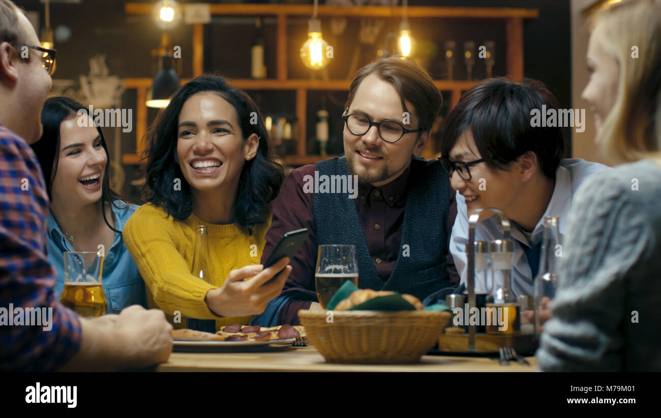 Schöne Hispanic Frau zeigt interessante Sachen auf Ihrem Smartphone zu Ihren Freunden während Sie gute Zeit in Bar. Sie Lachen, Scherzen, Getränk in der Bar Stockfoto