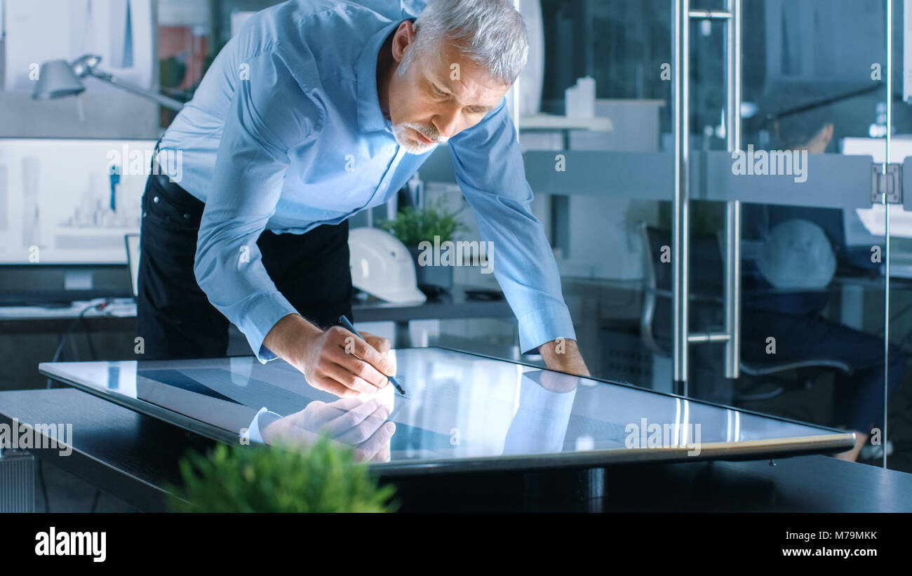 Senior architektonischer Ingenieur zeichnet Gebäude Konzept auf ein Grafiktablett Anzeige Vertikale Touchscreen Tabelle. Reinigen Sie minimalistisch Büro, Beton Wand Stockfoto