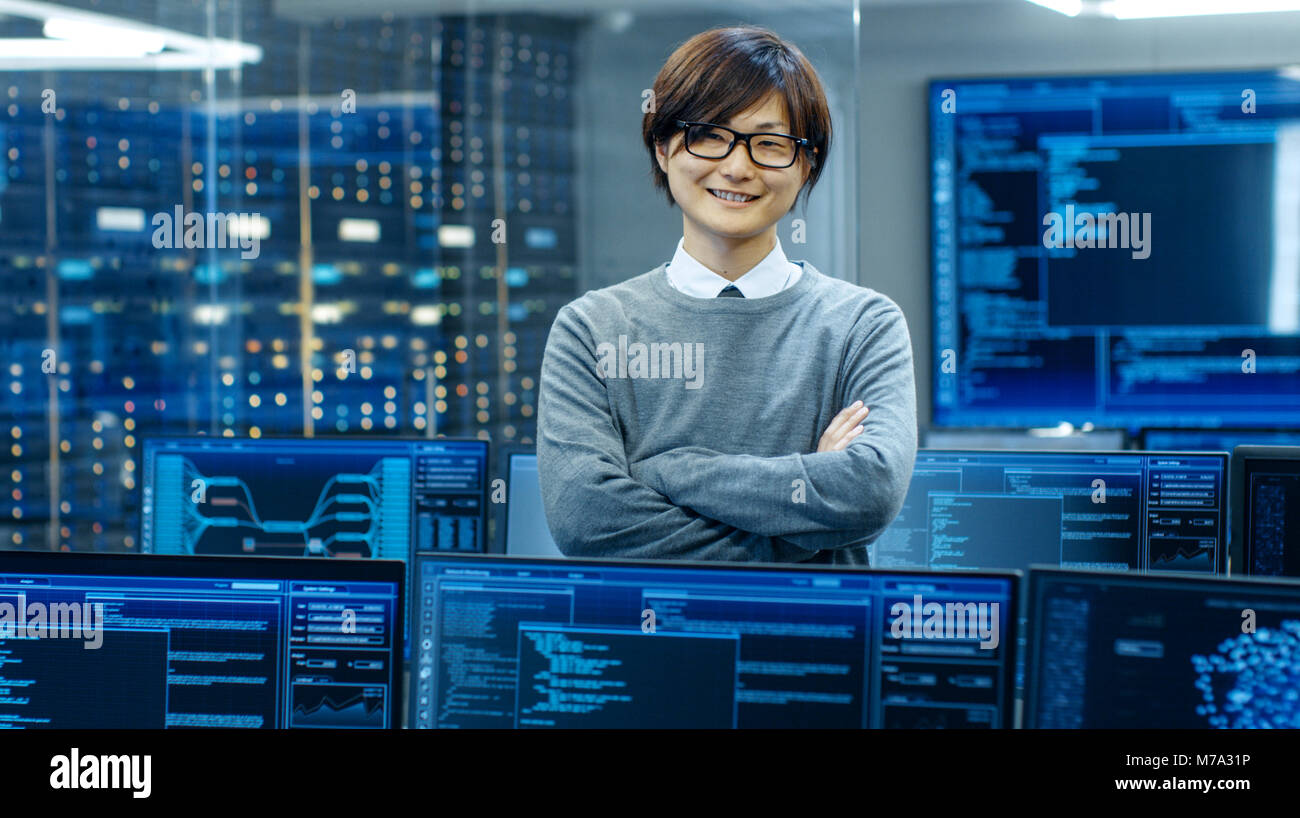 Im System Control Room IT-Techniker kreuzt die Arme und lächelt. Er ist durch mehrere Anzeigen für Grafiken umgeben. Stockfoto