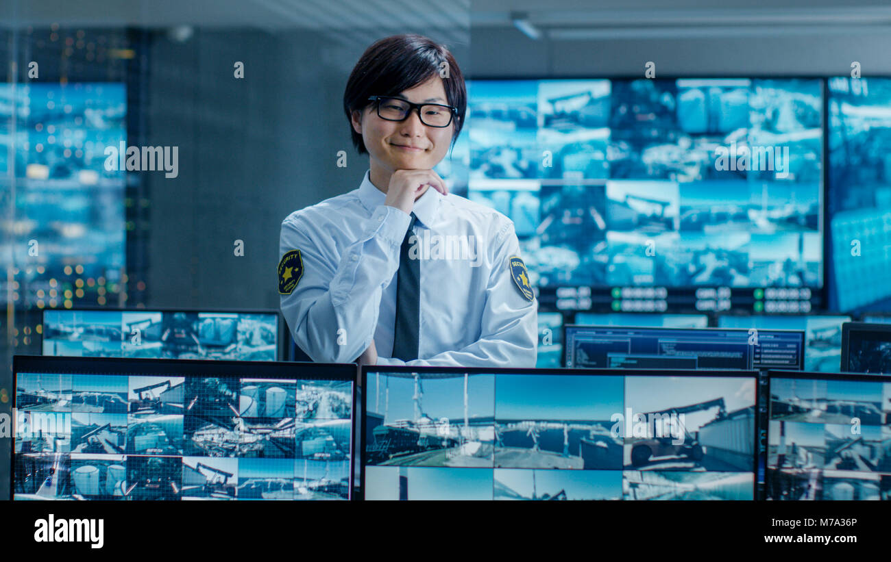 In den Sicherheitsraum Officer Monitore Bildschirme für verdächtige Aktivitäten, er lächelt in die Kamera. Bildschirme zeigen internationale Logistik. Stockfoto