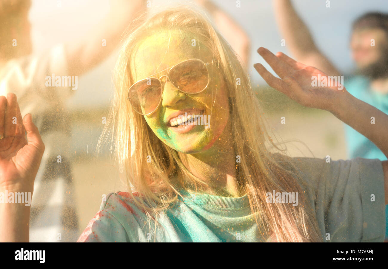 Porträt einer schönen blonden Mädchen tanzt in der Feier von Holi Festival mit Ihren Freunden. Ihr Gesicht und Kleidung sind mit farbenfrohen Pulver bedeckt. Stockfoto