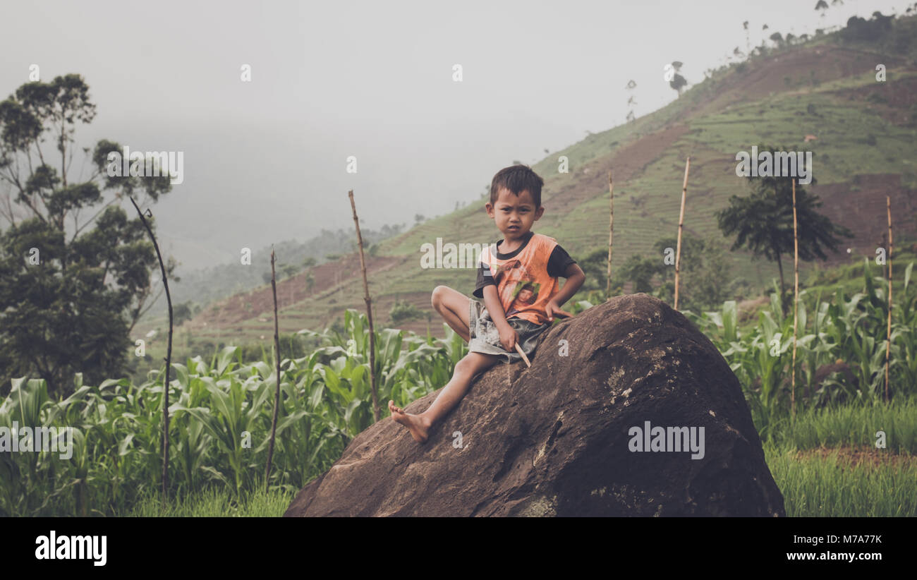 Ein Junge, der sich auf Rock, während seine Eltern Landwirtschaft Stockfoto