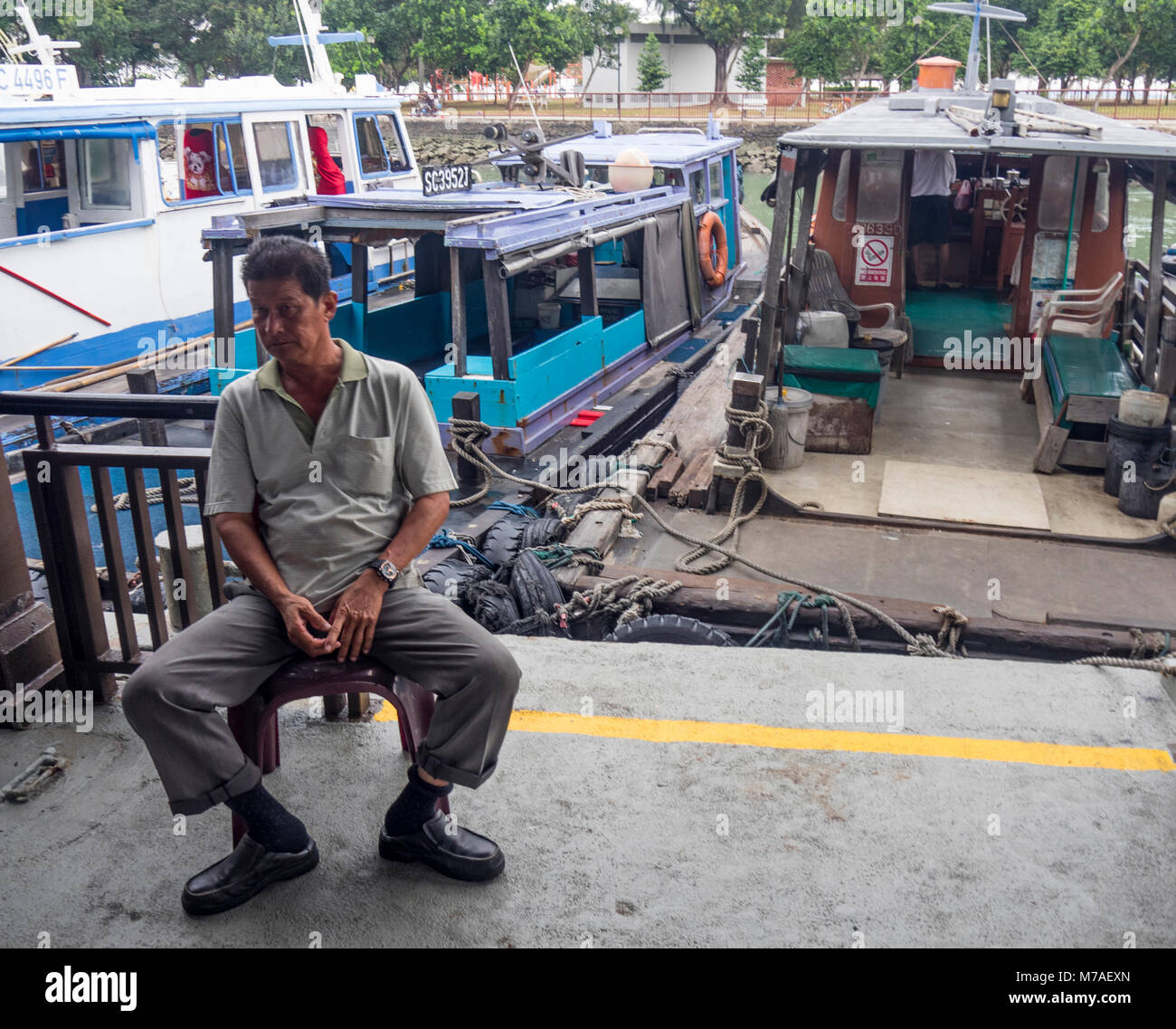 Ein Boot Besatzungsmitglied auf einem Stuhl sitzend Warten auf Passagiere aus Singapur in die Insel Pulau Ubin durch Bumboat oder dem Wassertaxi. Stockfoto
